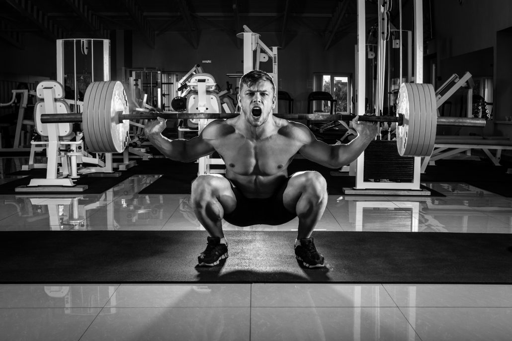 Man at the gym. Execute exercise squatting with weight, in gym